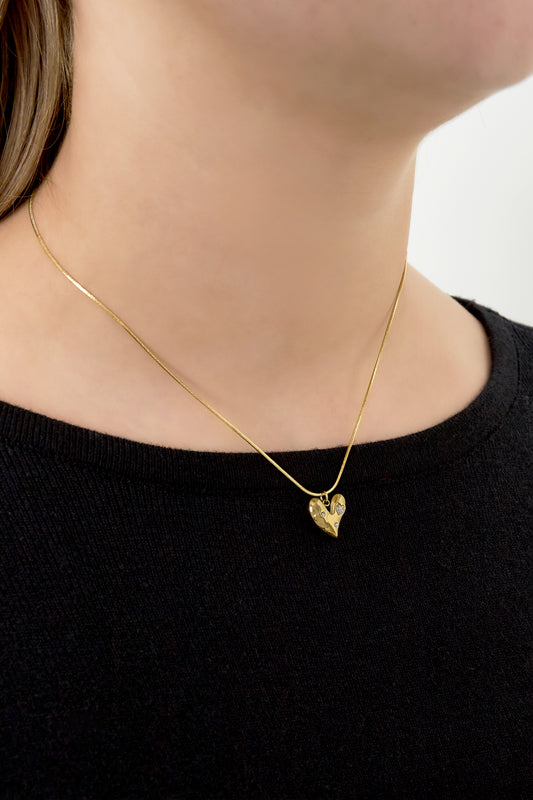 Close-up of a woman wearing a gold heart pendant necklace with rhinestones and a thin chain over a black top