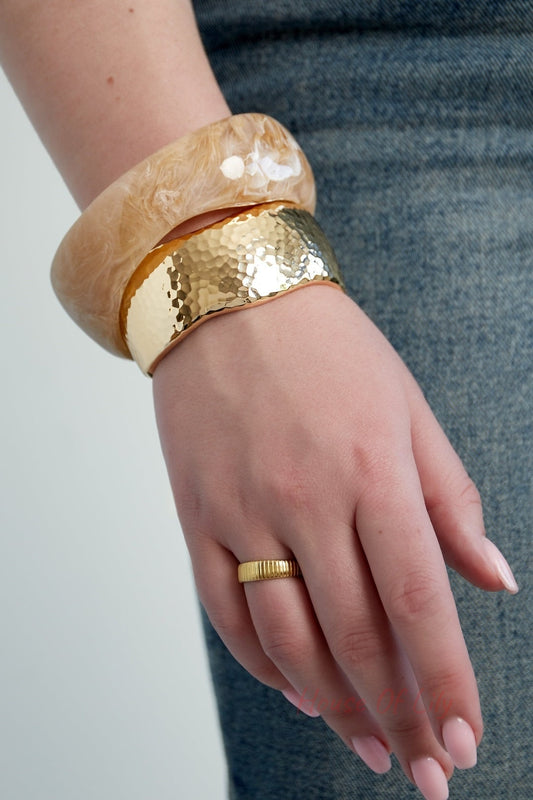 Woman wearing a beige marbled resin bangle and a gold-tone textured bangle with a gold ring, styled with denim