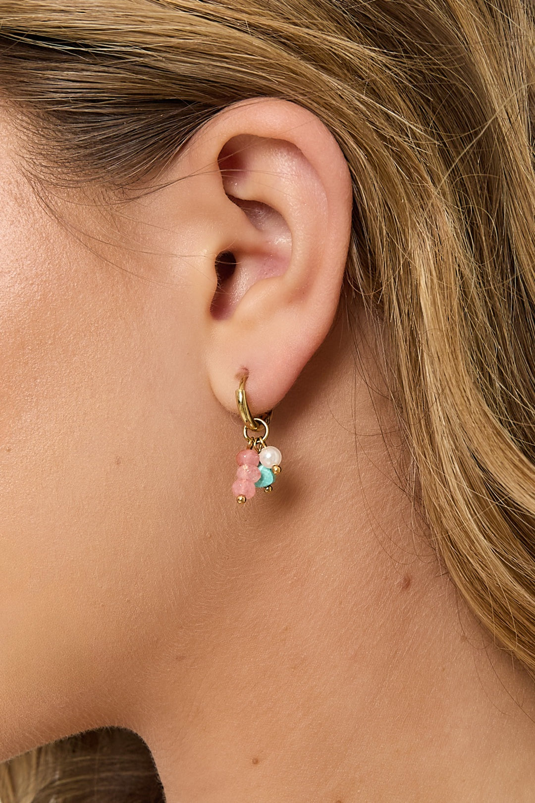 Close-up of a woman's ear showcasing gold hoop earring with pastel pink, turquoise, and pearl beads in a soft aesthetic style