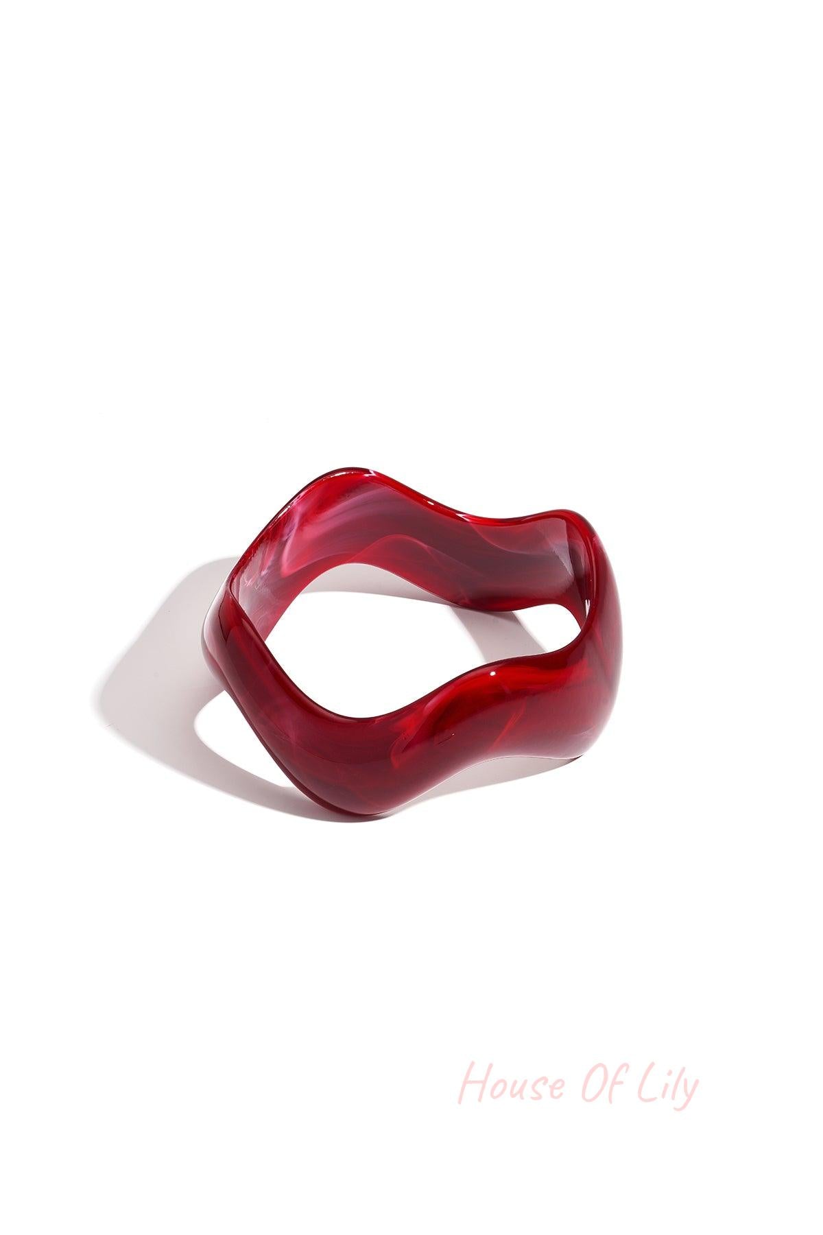 Red acrylic bangle with irregular wavy shape on white background