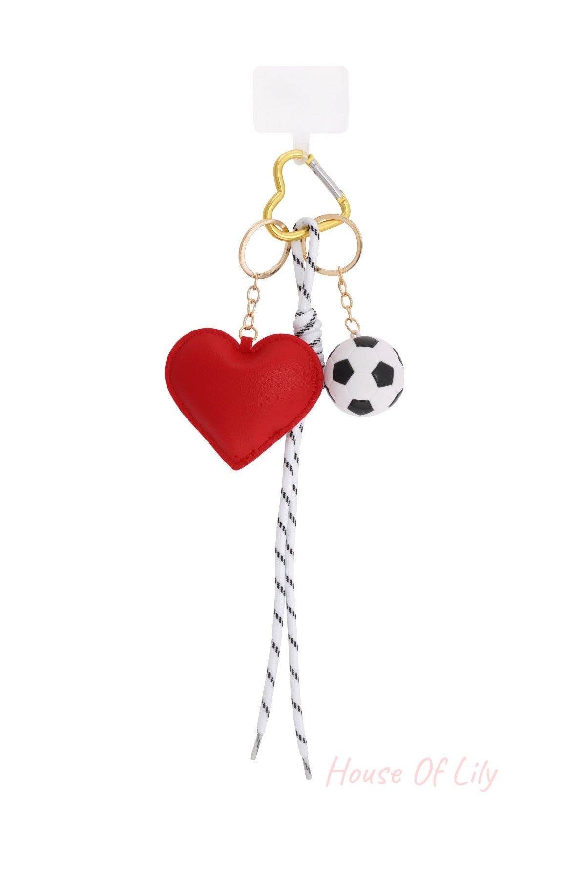 Close-up of a bag charm with red faux leather heart, black and white soccer ball, striped shoelace, and gold-tone heart shaped clip on white background