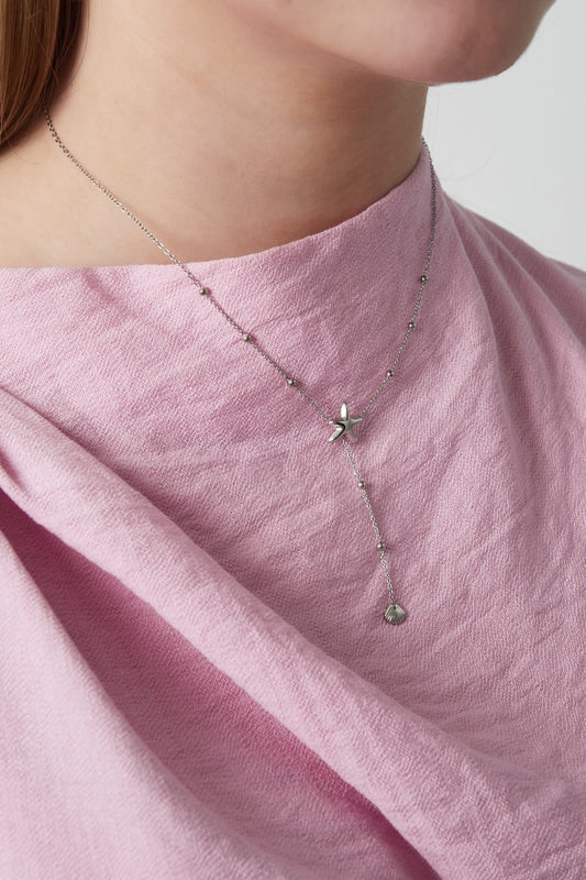 Close-up of woman wearing silver starfish necklace with pink fabric background, highlighting pendant and chain details