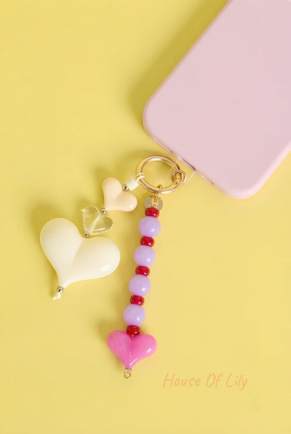 Pink and red heart bead bag charm attached to a phone with cream heart accents on yellow background