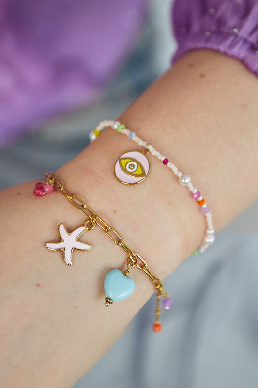 Close-up of wrist wearing pastel beaded bracelet with colorful beads and gold-tone eye charm paired with another gold charm bracelet