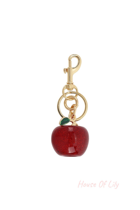 Close-up of a sparkling red apple bag charm with green leaf and gold lobster clasp on white background