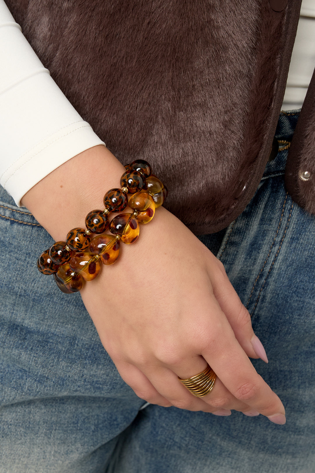 Woman wearing two stretch beaded bracelets including a leopard print heart-shaped amber bracelet paired with a gold ring and casual outfit