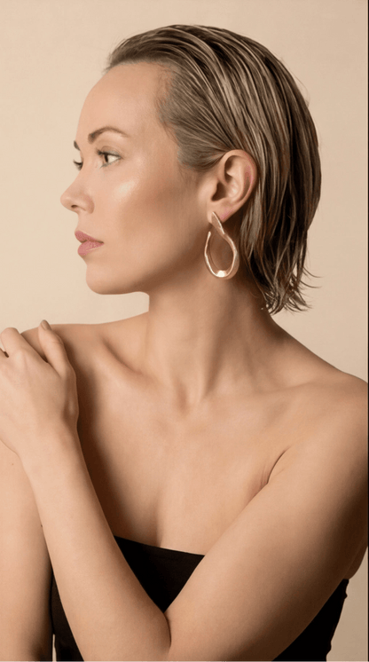Woman wearing gold hoop earrings against a beige background
