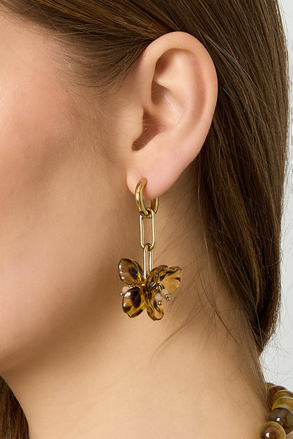 Close-up of model’s ear showcasing gold-tone hoop earrings with amber acrylic floral drop design