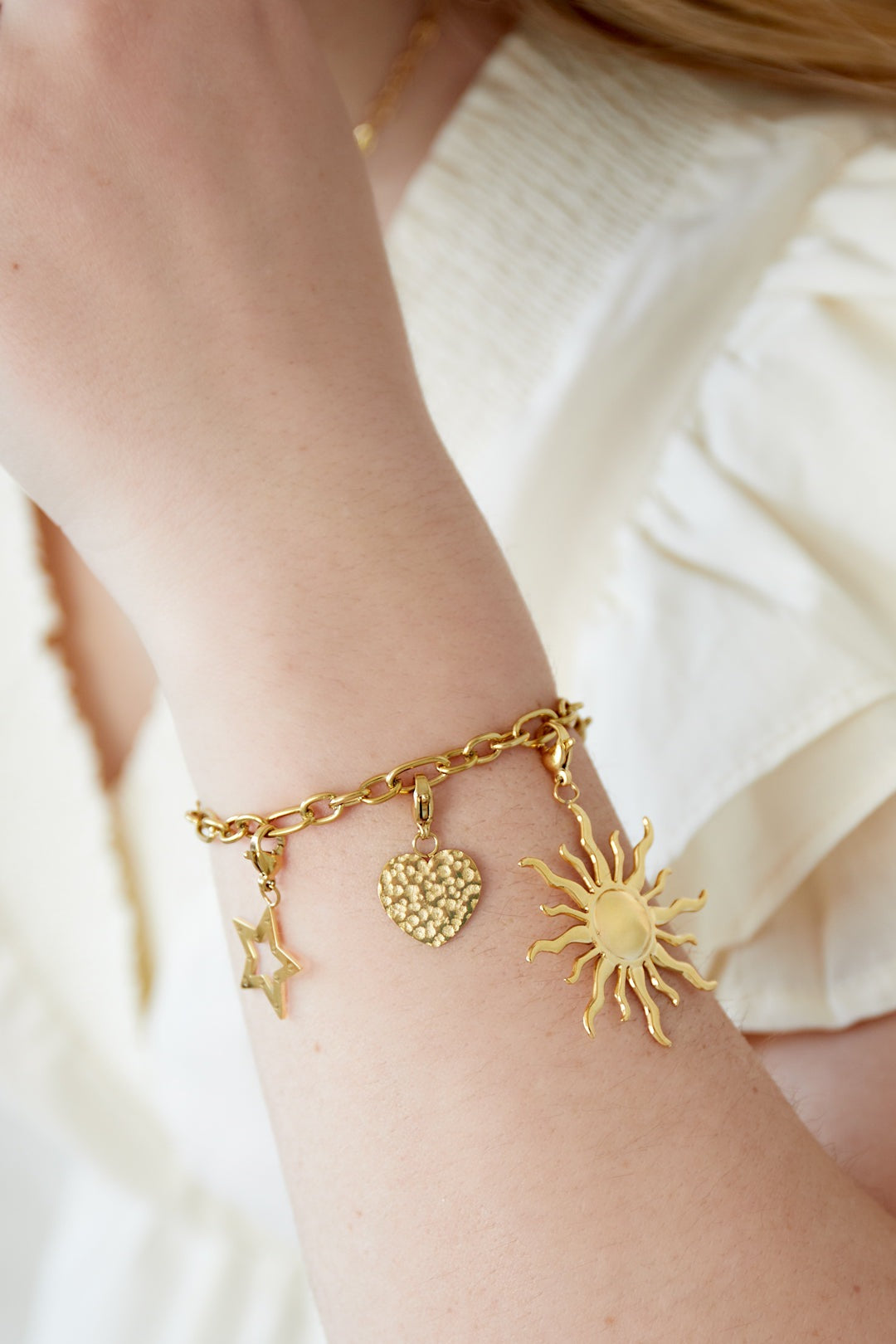 Woman wearing gold charm bracelet with sun, star, and heart charms paired with white ruffled top