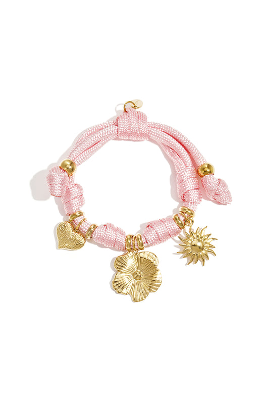 Pink rope charm bracelet with gold heart, flower, and sun charms on a white background