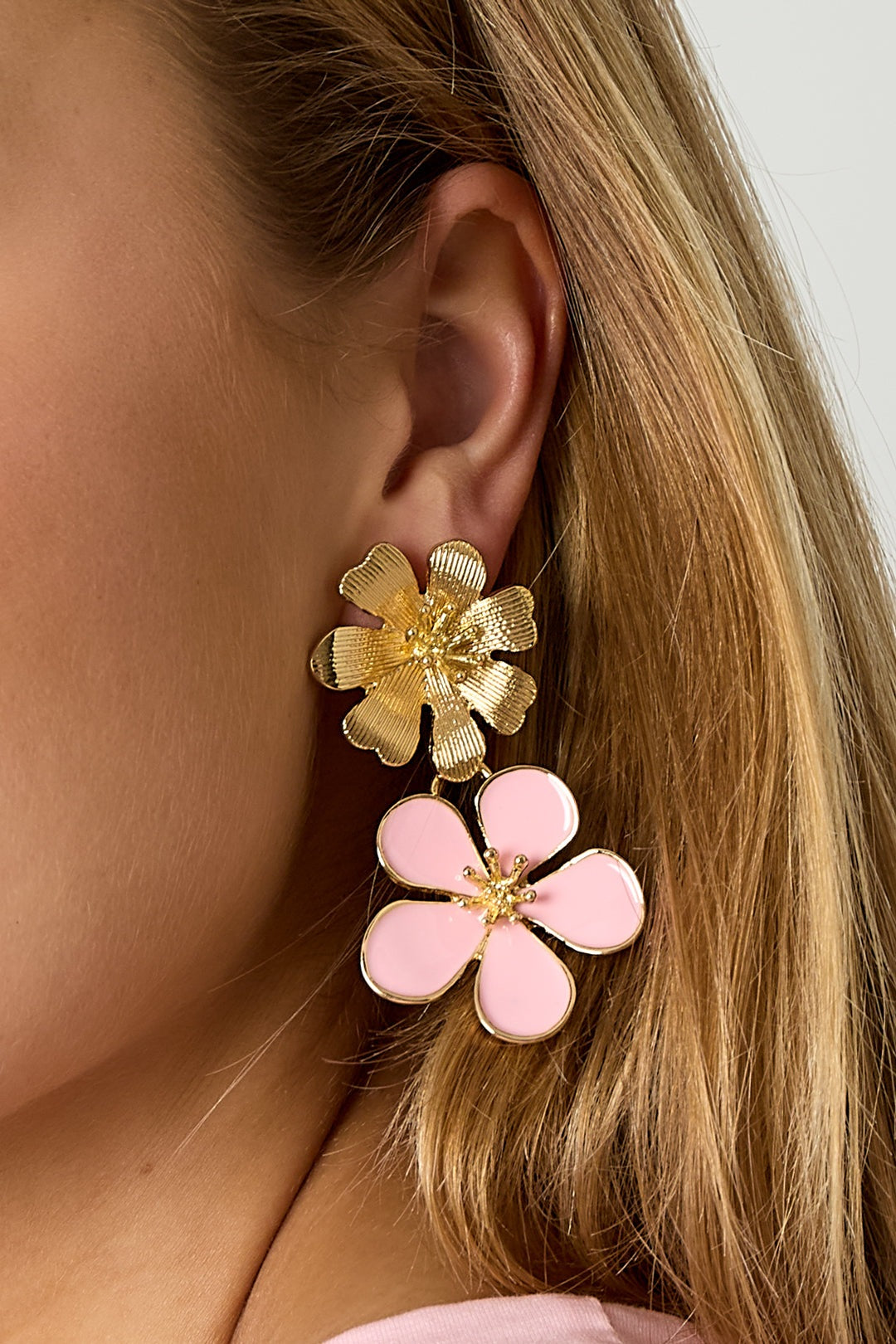 Close-up of model's ear wearing pink enamel flower and gold textured flower drop earrings