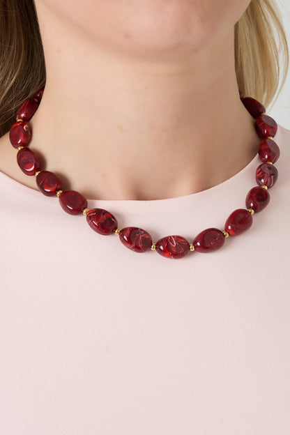 Woman wearing a red acrylic beaded necklace with gold spacer beads paired with light pink top