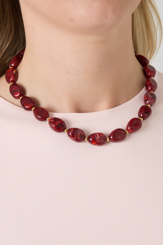 Woman wearing a red acrylic beaded necklace with gold spacer beads paired with light pink top