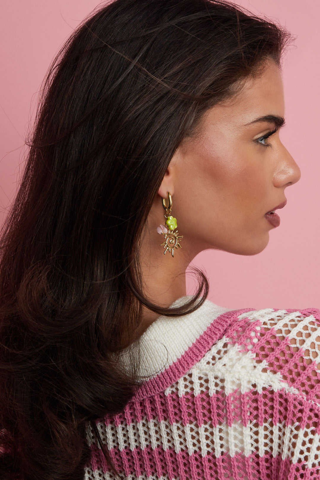 Model wearing gold-tone drop earrings featuring a sun charm, green four-leaf clover, and pink beads against a pink background