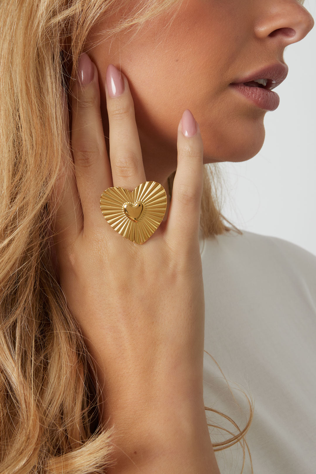 Female model wearing the gold heart statement ring on her finger showing a soft, youthful look