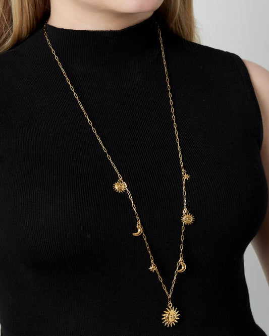 Gold necklace with star-shaped pendants on a black sleeveless top against a neutral background