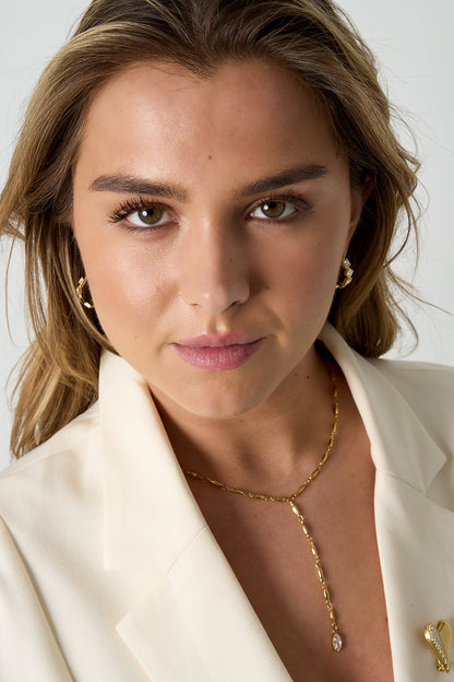 Close-up of front-facing model wearing gold square rhinestone hoop earrings, cream blazer, and gold chain necklace