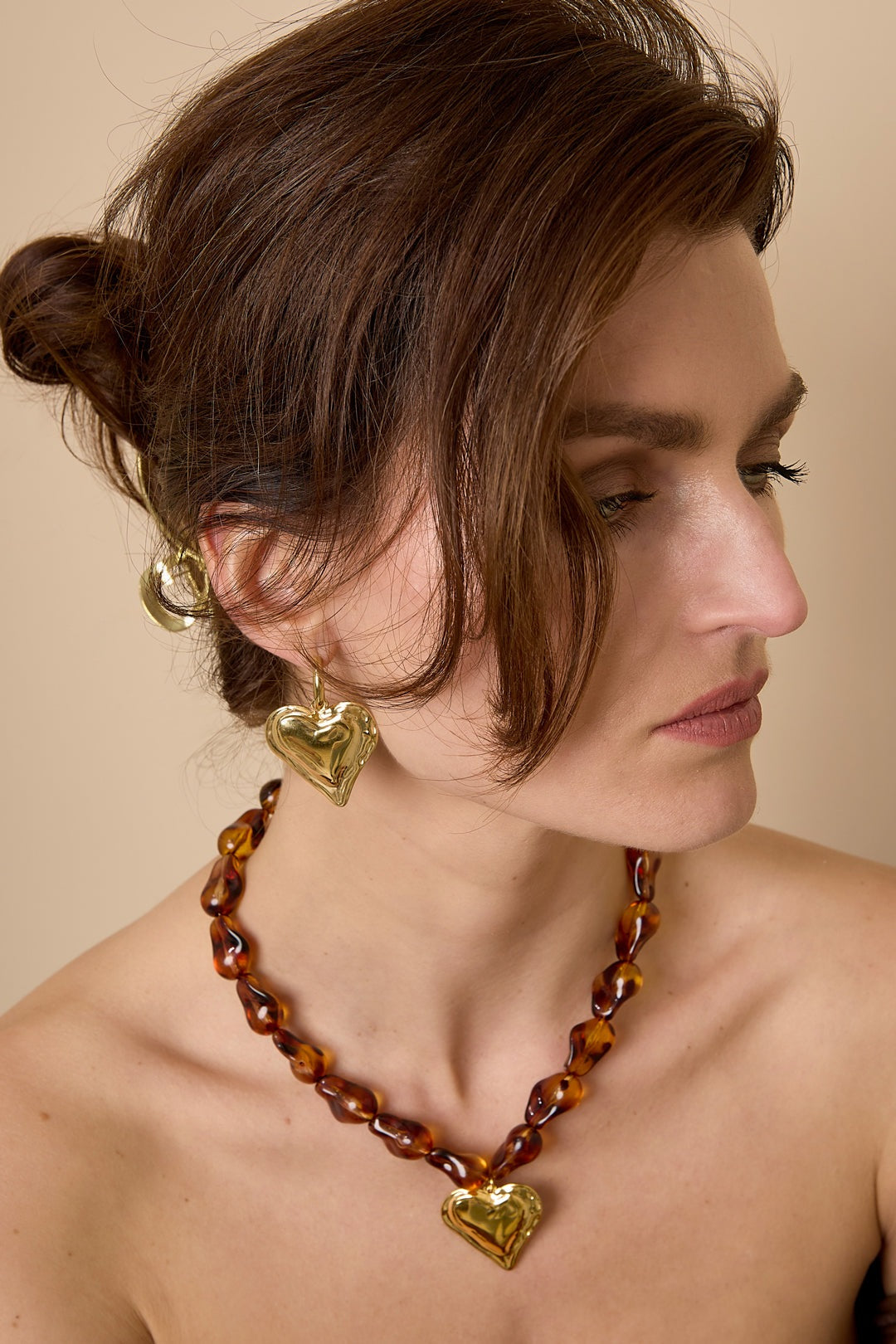Model wearing chunky gold heart hoop earrings paired with matching heart pendant necklace and brown beaded chain