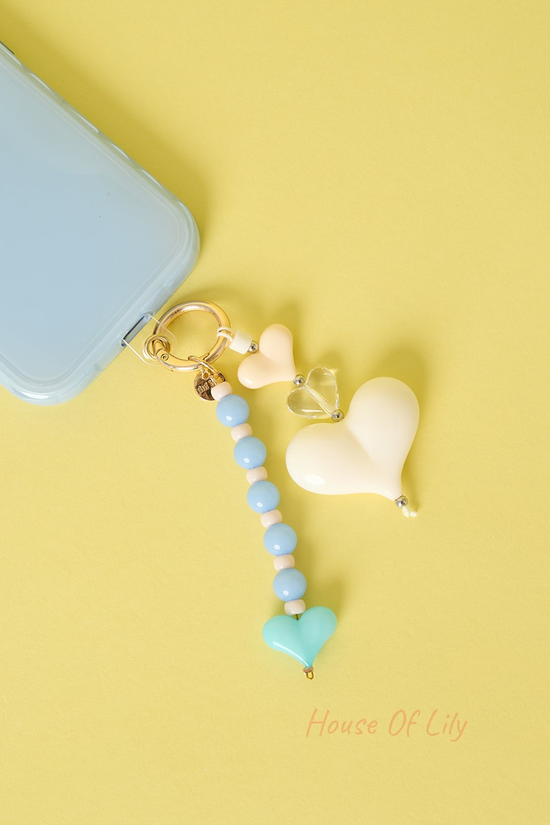 Multicolor heart charm keychain attached to blue phone case on bright yellow background featuring pastel and clear acrylic hearts with blue beads