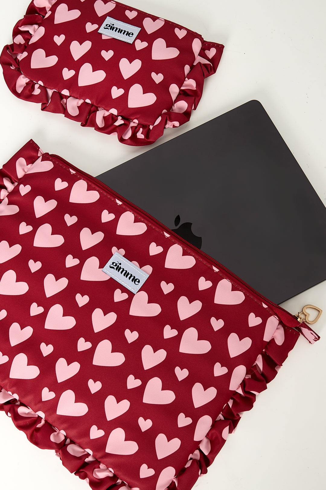 Red laptop sleeve and matching pouch with pink hearts, showing laptop partially inside and heart-shaped zipper pull