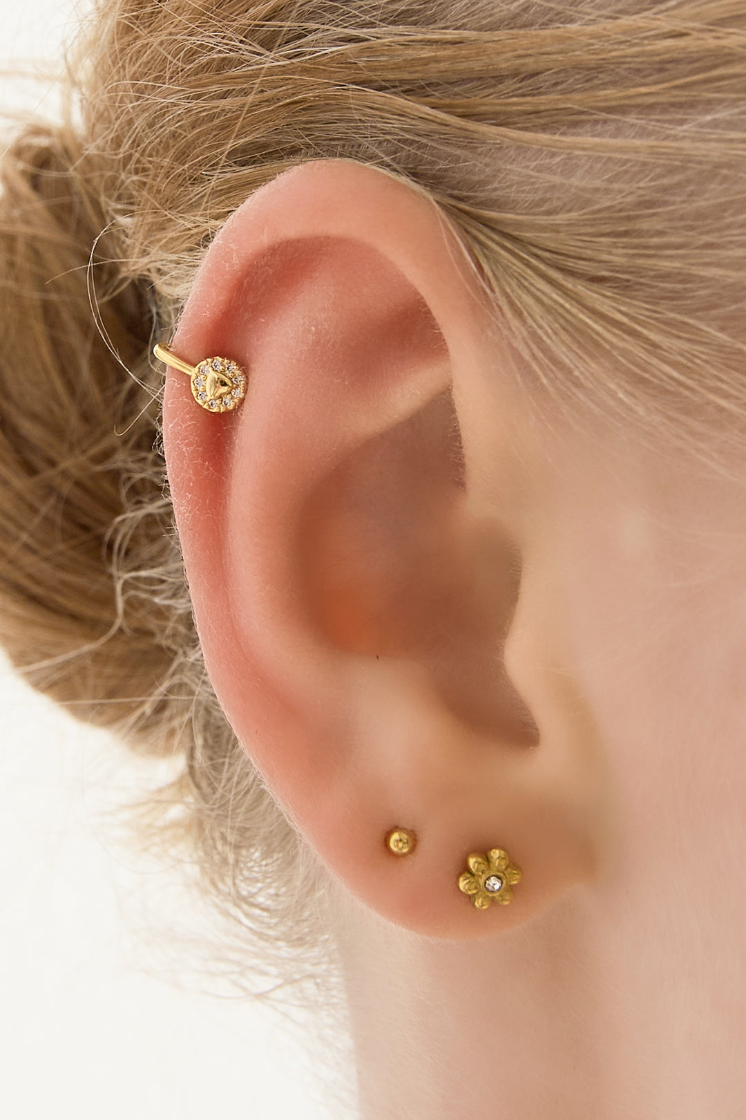 Close-up of a woman wearing the gold-toned triangle zircon ear cuff on her ear with other small gold earrings