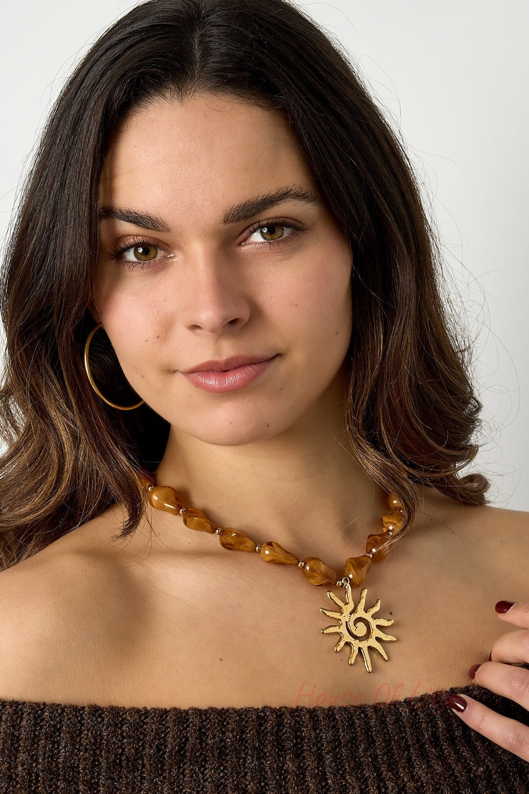 Model wearing the caramel brown acrylic beaded necklace with gold sun pendant paired with a brown off-shoulder sweater