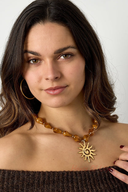 Model wearing the caramel brown acrylic beaded necklace with gold sun pendant paired with a brown off-shoulder sweater