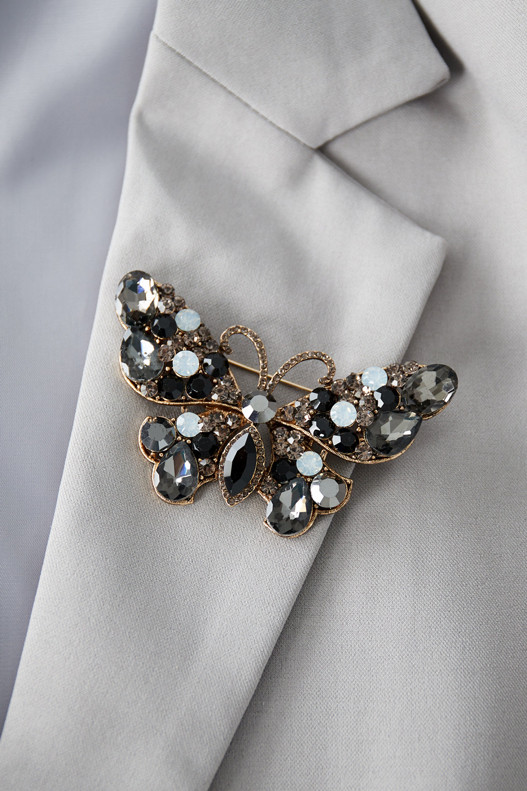 Smoky gray and black butterfly brooch pinned on a light gray blazer lapel