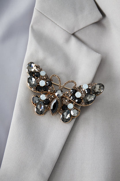 Smoky gray and black butterfly brooch pinned on a light gray blazer lapel