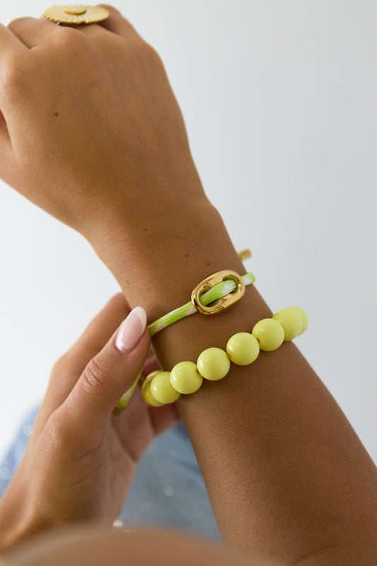 Vibrant chunky clasp bracelet featuring a lime green cord, gold oval link, and a stack of yellow beads on a wrist.