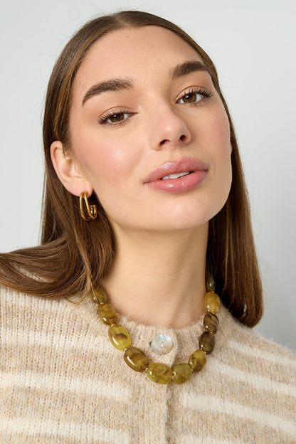 Model wearing amber beaded necklace with gold hoop earrings and beige striped sweater