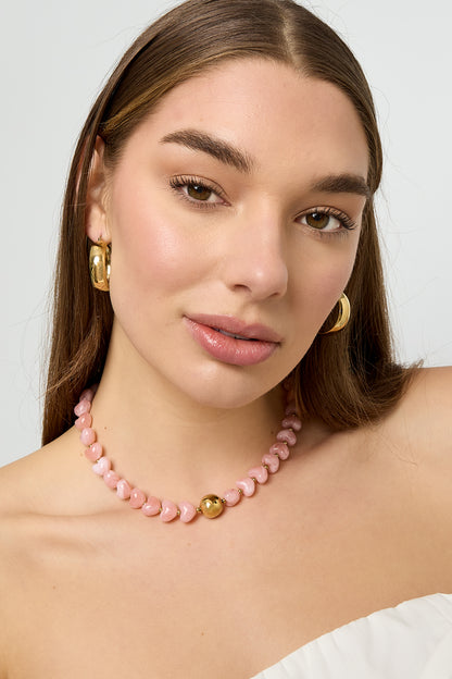 Model wearing the pink heart-shaped beaded necklace with gold round bead, paired with gold hoop earrings and white off-shoulder top