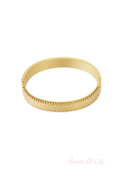 Close-up of gold chevron patterned bangle bracelet with beaded edges on white background