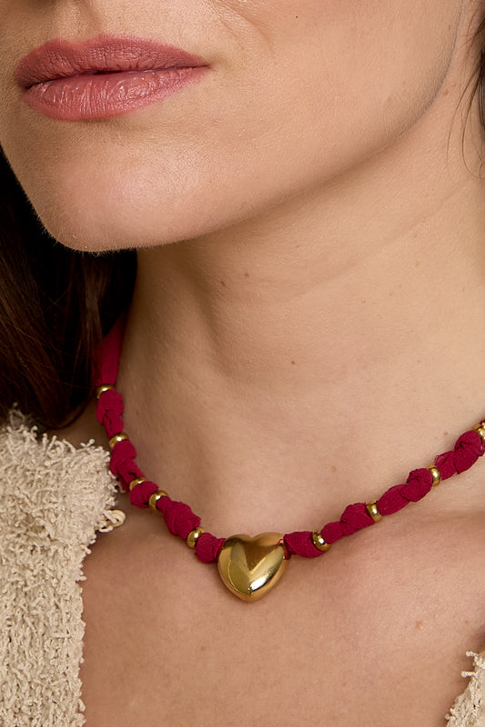 Close-up of woman’s neck wearing gold heart pendant necklace with burgundy braided fabric