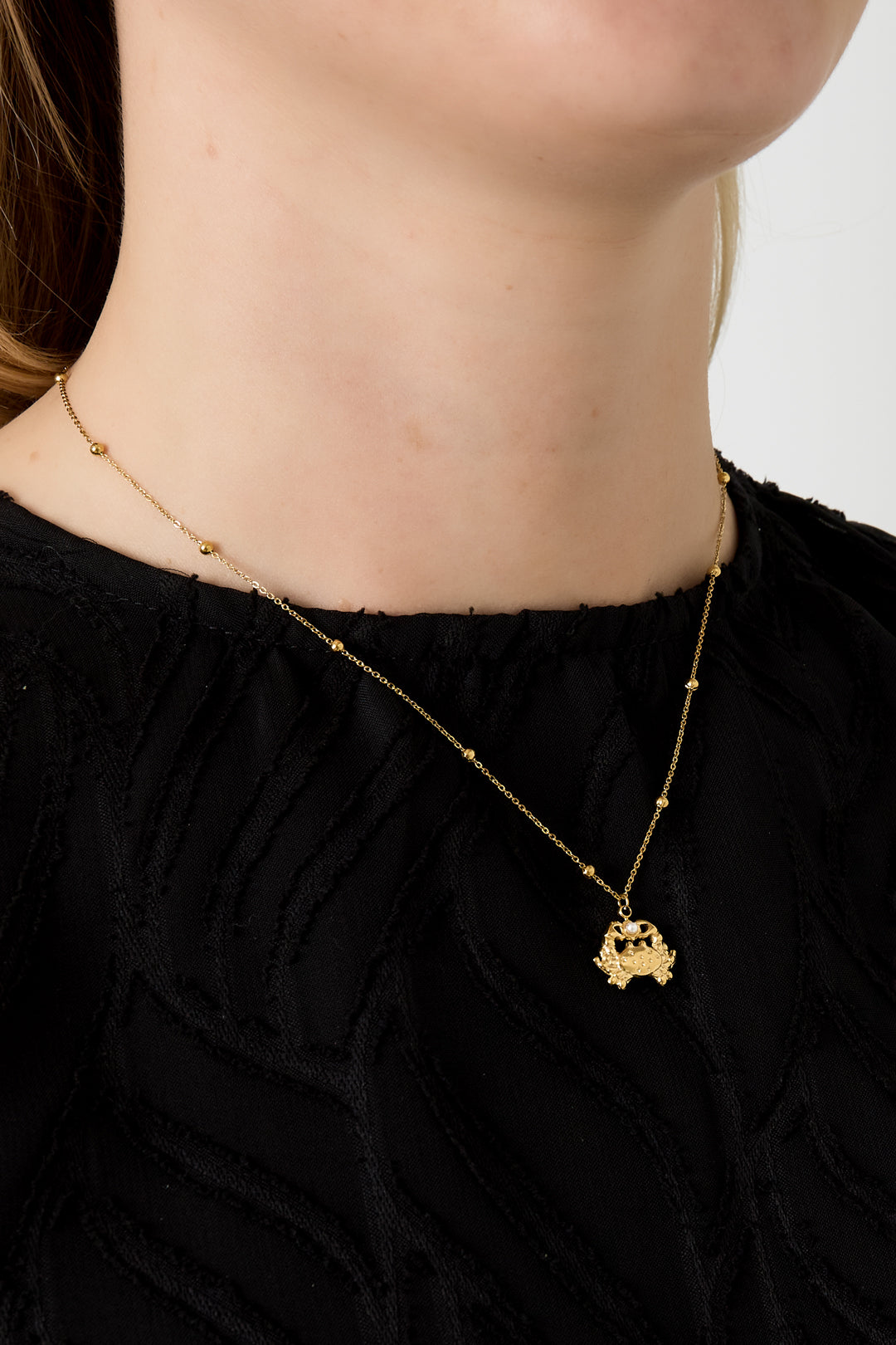 Model wearing gold crab charm necklace with beaded chain and black top