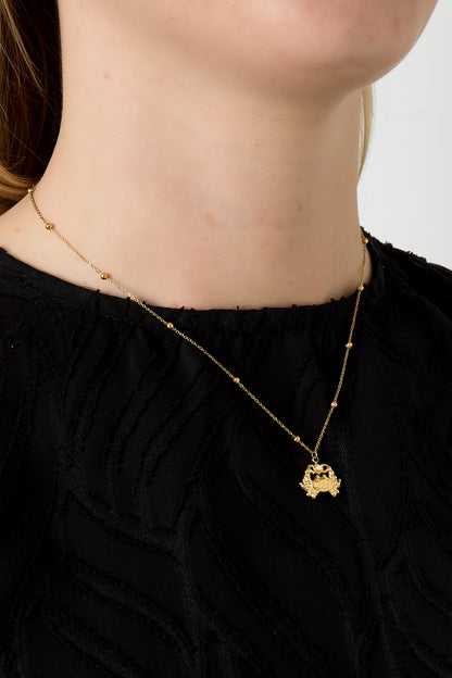 Model wearing gold crab charm necklace with beaded chain and black top