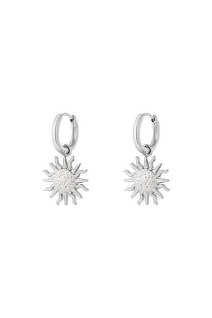 Pair of silver drop hoop earrings with textured sun charm pendants on white background