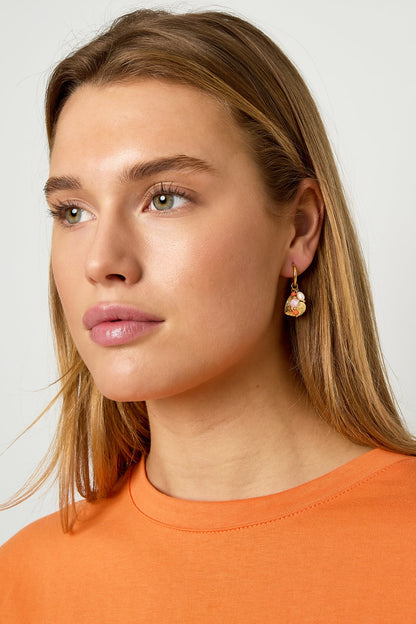 Close-up of woman wearing gold heart hoop earring with pearl and bead charms, styled with orange top