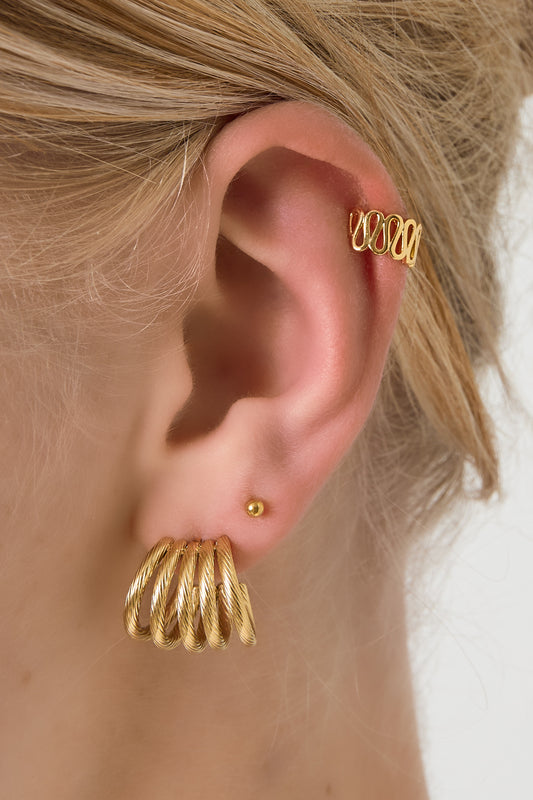Model wearing gold swirl ear cuff on upper ear, paired with gold hoop and stud earrings