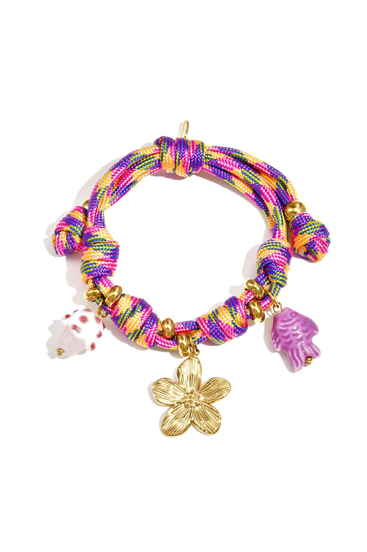 Multicolor woven rope charm bracelet with gold flower, cupcake, and purple fish charms on white background