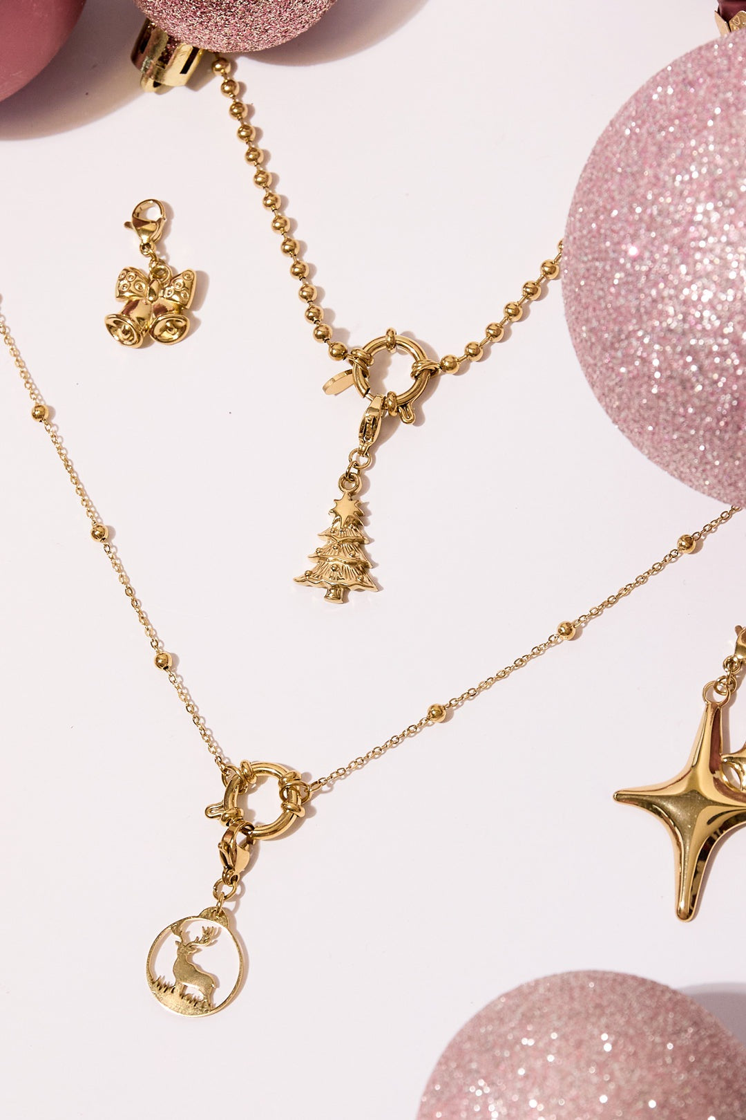 Festive arrangement of gold tone Christmas tree charm attached to delicate gold chain, surrounded by pink glitter ornaments and other holiday charms
