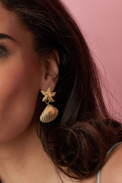 Model showcasing one golden starfish shell drop earring against pink background