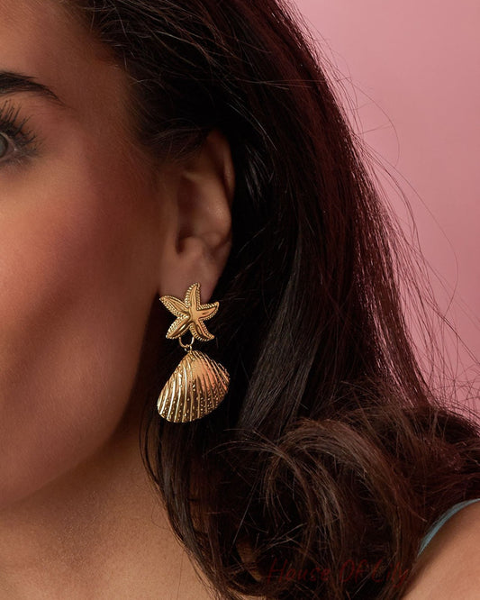 Model showcasing one golden starfish shell drop earring against pink background