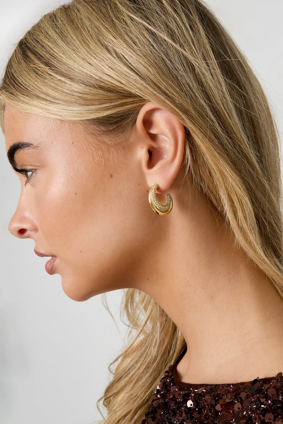 Profile view showing gold tone rhinestone hoop earring on woman with blonde hair