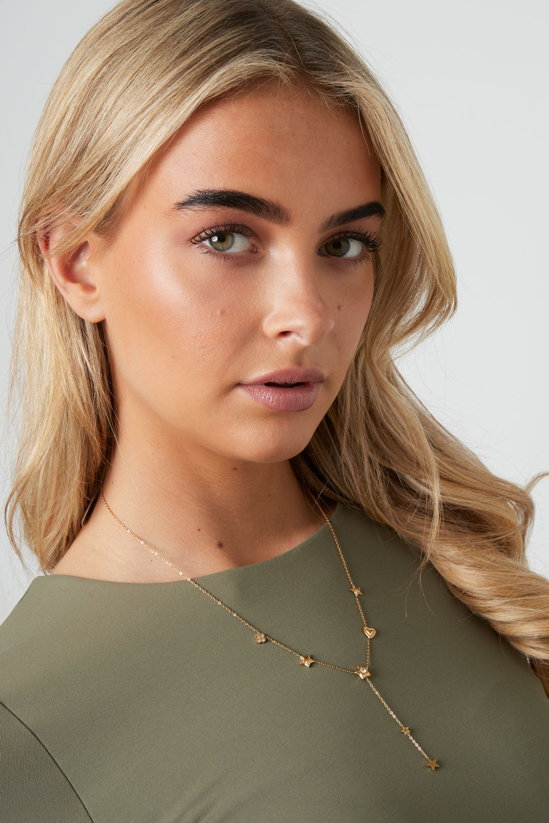 Close-up of a woman with blonde hair wearing the gold star and heart pendant necklace paired with olive green top