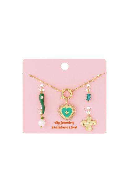 Gold stainless steel necklace with a green enamel heart charm and assorted decorative charms on a pink display card.