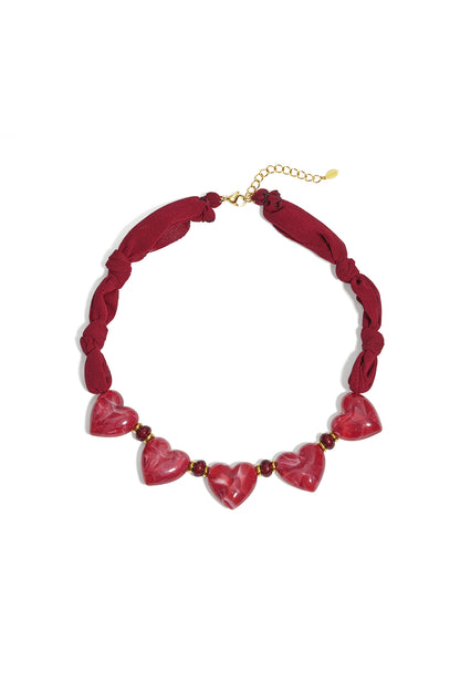 Close-up image of a burgundy fabric necklace with five glossy red heart-shaped beads and gold accents