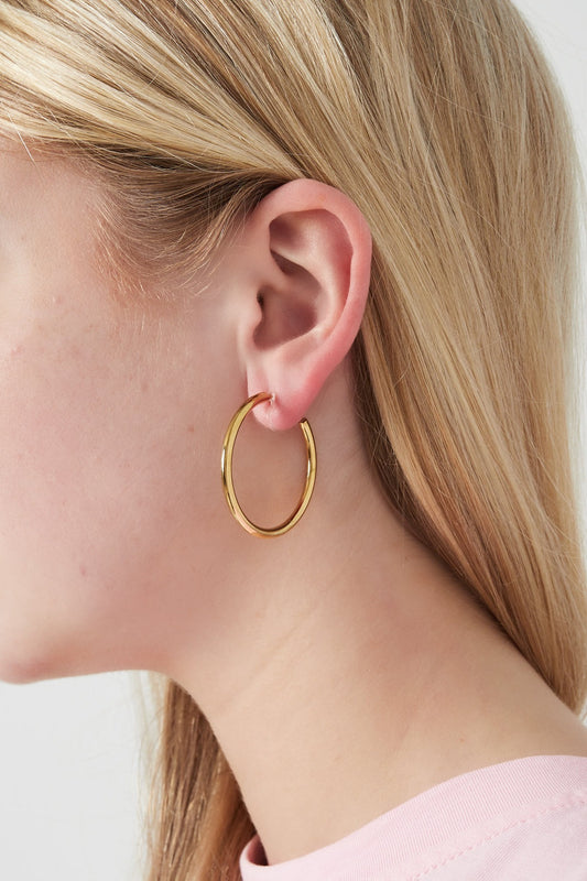 Close-up side view of a woman's ear wearing a gold clip-on hoop earring showcasing size and fit
