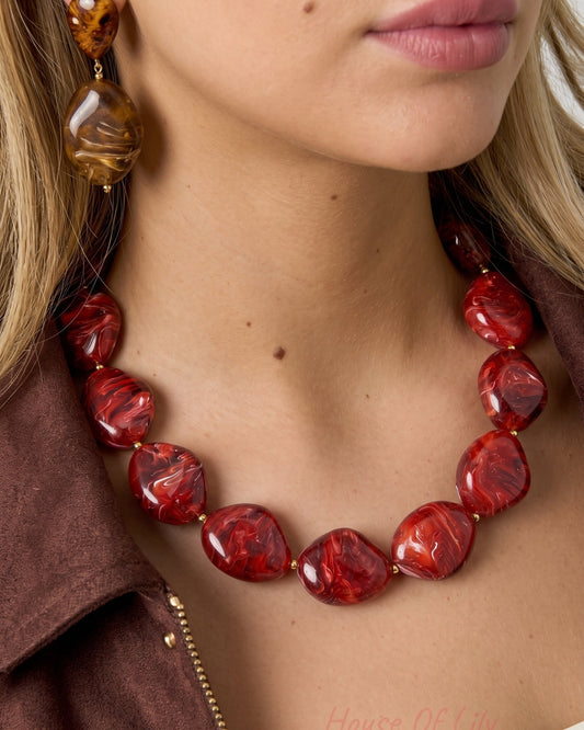 A model wears a polished acrylic beaded necklace in swirled shades of red, with matching amber-toned drop earrings.