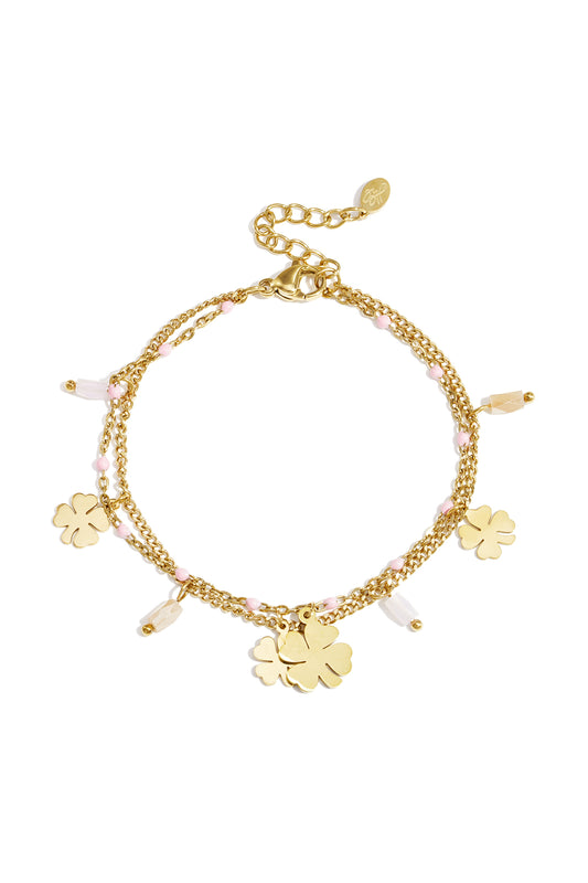 Gold-tone double chain charm bracelet adorned with pink beads and four-leaf clover pendants laid flat